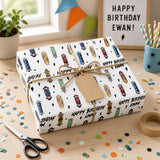 A birthday gift wrapped in a white paper with a skateboard pattern, sitting on a table surrounded by confetti. There is a pair of scissors and a roll of tape nearby.