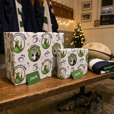 A pair of rugby-themed gift boxes with the name "Jack" printed on them, placed on a wooden bench in a room decorated with Christmas lights and a Christmas tree.