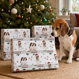 A beagle dog sits in front of a Christmas tree, surrounded by wrapped presents with a festive design.