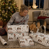 A woman in a grey sweater sits on the floor surrounded by Christmas presents, with a beagle dog standing nearby.