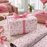 a gift box with a pink ribbon and a pink bow, placed on a table with a glass of champagne and confetti.