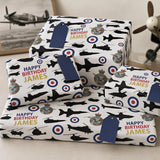 several wrapped gifts with a military theme, featuring images of airplanes and other military equipment. The gifts are labeled "Happy Birthday James" and are arranged on a surface.