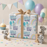 a birthday gift wrapped in a white paper with a blue and white design, surrounded by balloons and figurines, with the text "Happy 1st Birthday Oliver" on it.