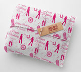 The image is a gift wrapped in pink paper with a repeating pattern of silhouettes of people and horses, along with the text "Happy Birthday Nadia". The paper has a brown tag that says "HOT OFF THE PRESS".