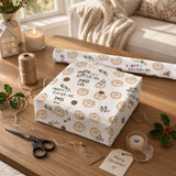 a festive scene with a wrapped gift box adorned with a pattern of cute cartoon faces, a pair of scissors, a roll of tape, and a card with a message.