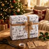 A gift box wrapped in a football-themed wrapping paper sits on a wooden table, with a pair of scissors and a Christmas tree visible in the background.