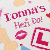 a close-up of a personalized birthday card with the name "Donna's Hen Do!" printed on it. The card also features various other elements such as a pink lipstick, a heart, and a letter "L".