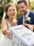 A bride and groom are holding a wedding gift box together, smiling and appearing happy.