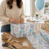 A woman is wrapping a birthday gift box with a "Happy 1st Birthday Noah" theme, surrounded by party supplies and decorations.