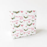 The image is a square-shaped gift box with a repeating pattern of Christmas-themed elements, including a Christmas tree, holly leaves, and wine glasses. The text "Merry Christmas Alena" is printed on the gift box in a festive style.