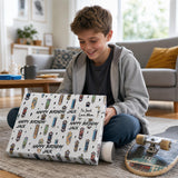 A young boy sits on the floor, smiling as he opens a skateboard-themed birthday gift.