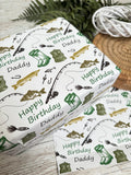 a gift box with a fishing theme, decorated with illustrations of fishing rods, fish, and other fishing-related items. The box is placed on a wooden surface, and there is a wicker basket nearby.