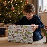 A young boy in blue pajamas is excitedly opening a gift box with a dinosaur theme, surrounded by a Christmas tree and other holiday decorations.
