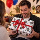 A man is holding a gift wrapped in a dartboard-themed wrapping paper with a red ribbon, smiling as he presents it to another person.