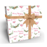A gift box with a Christmas-themed wrapping paper featuring a repeating pattern of wine glasses, pine cones, and greenery. The gift box is tied with a brown bow.