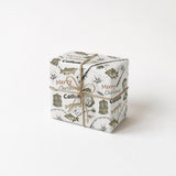 A gift box wrapped in a white paper with a repeating pattern of Christmas-themed illustrations, tied with a twine bow.