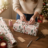 A woman is wrapping a Christmas gift on a wooden table, surrounded by wrapping paper, scissors, and other holiday decorations.
