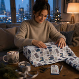 A woman in a beige sweater is wrapping a gift with a patterned wrapping paper, surrounded by holiday decorations and a mug of hot chocolate on a wooden table.