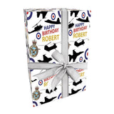 A gift box with a white background and a gray ribbon tied around it. The gift box has a pattern of military aircraft and the text "Happy Birthday Robert" printed on it.