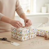 A person is wrapping a gift box with a patterned wrapping paper featuring cartoon animal designs.