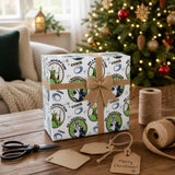 A Christmas-themed gift box with rugby-related designs sits on a wooden table, surrounded by holiday decorations and a pair of scissors.
