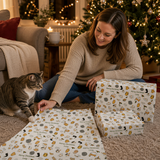 A woman sits on the floor in front of a Christmas tree, surrounded by wrapped presents and a cat.