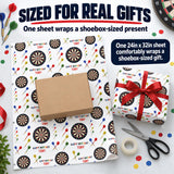 a variety of items related to gift wrapping, including a 24in x 32in sheet of wrapping paper with a dartboard pattern, a brown cardboard box, scissors, and a red ribbon.