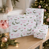 a festive scene with Christmas decorations, including a Christmas tree, a vase, and a wine glass. There are three wrapped gifts with a pattern of Christmas trees and greenery, and a pink drink in a glass.