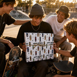 A group of young men are gathered around a young man who is holding a skateboard-themed gift box, all smiling and appearing to be enjoying the moment.