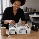 A woman is smiling and wrapping a gift with a patterned wrapping paper that includes a character design.