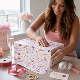 A woman in a pink dress is smiling and opening a gift box with a floral pattern.
