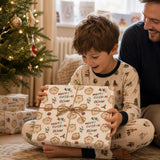A young boy in pajamas is excitedly opening a Christmas gift, while a man in a blue shirt watches on.