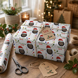 A festive Christmas gift wrapped in a patterned wrapping paper with a dartboard design, along with a tag that says "Merry Christmas CATH". The gift is placed on a wooden table, with a pair of scissors and some holiday decorations visible in the background.