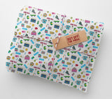 a gift wrapped in a paper with a repeating pattern of 90s-themed icons, including a skateboard, telephone, and various other objects. The paper has a brown tag that says "HOT OFF THE PRESS".